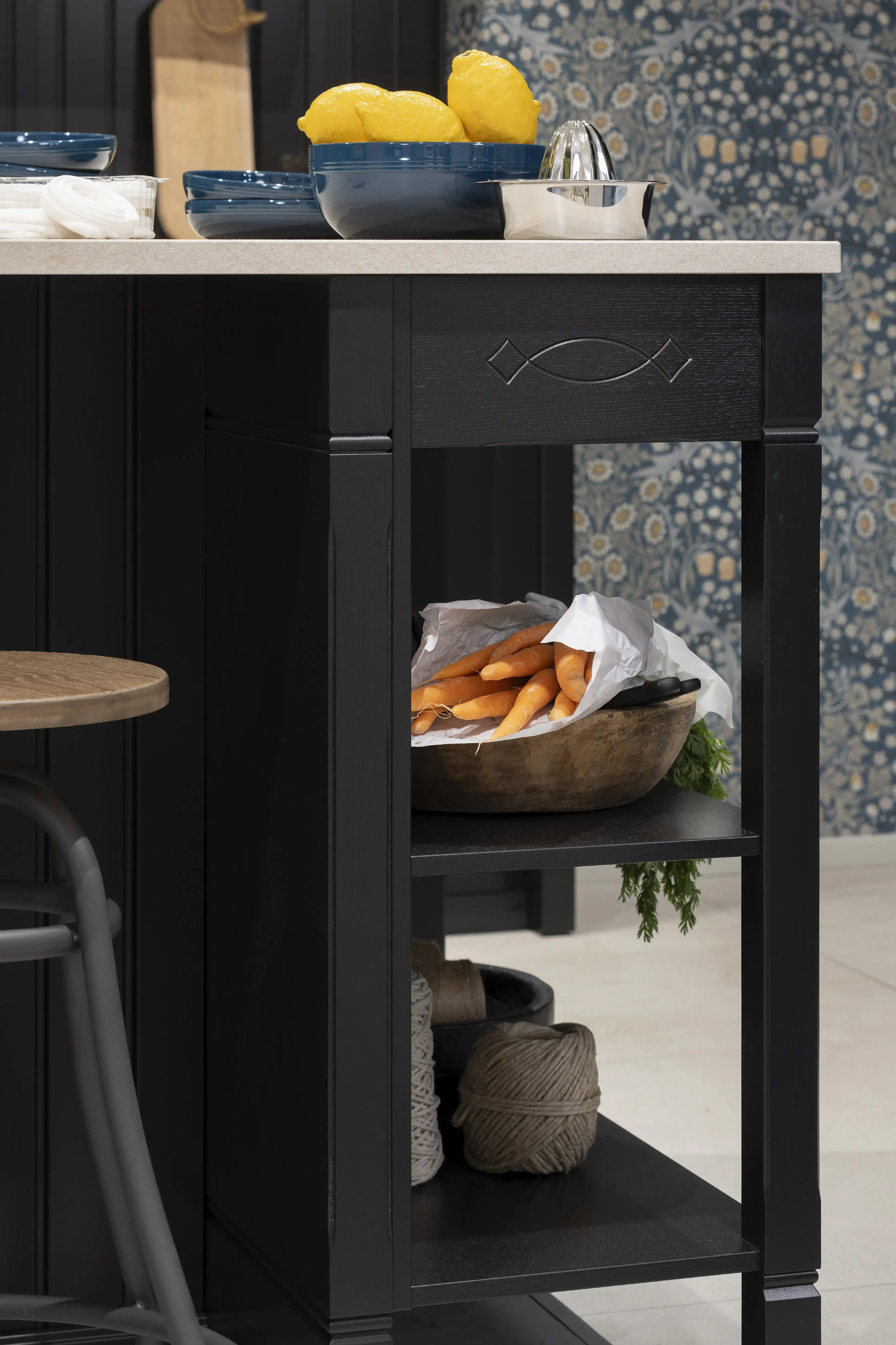 Schwarzer Küchenschrank mit Karotten auf der Regal und blaue Schalen und Zitrone auf der Arbeitsplatte.