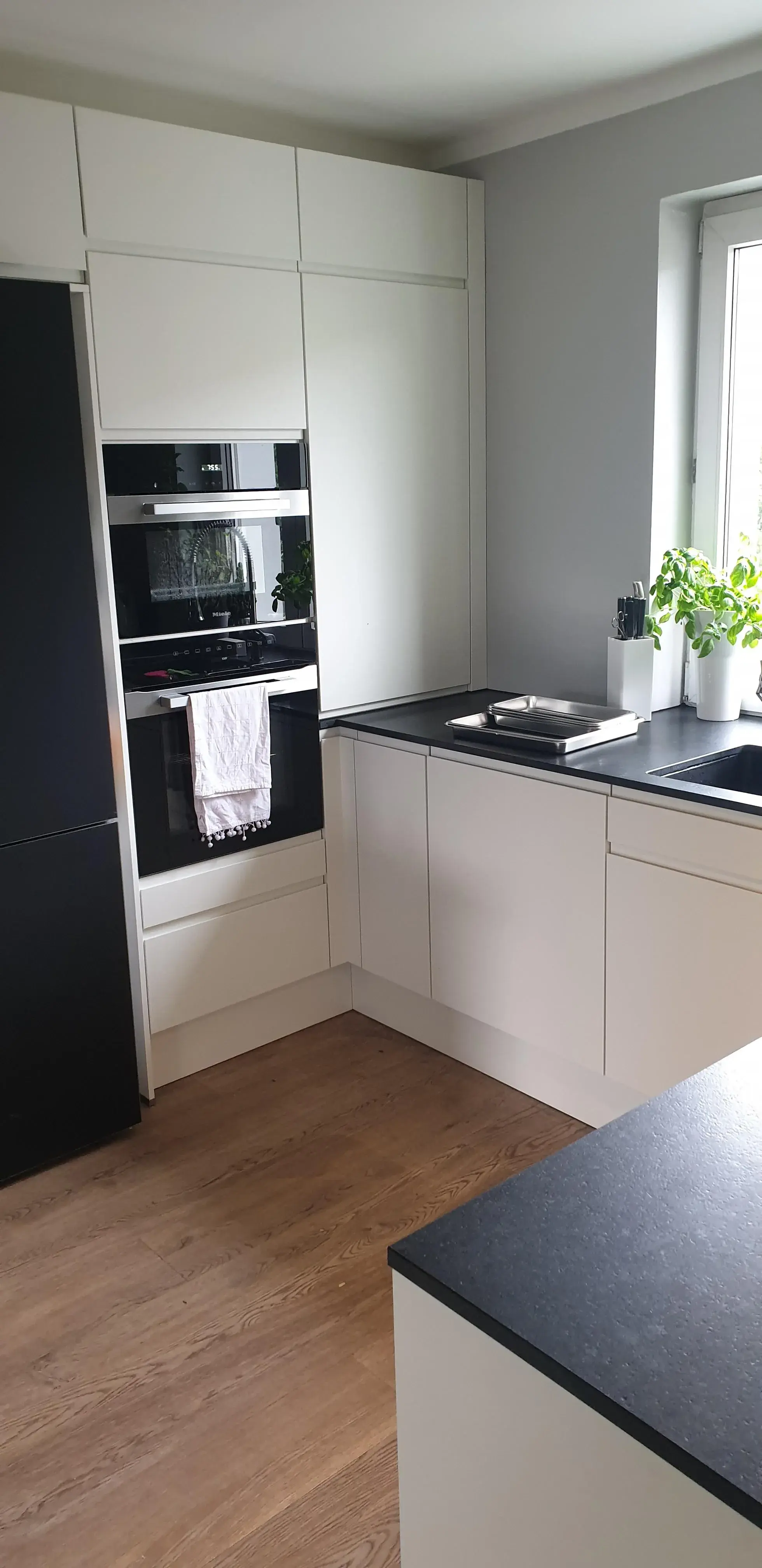 Moderne Einbauküche mit weißen grifflosen Fronten, schwarzer Arbeitsplatte, Miele-Einbaugeräten und großzügigem Hochschrank.