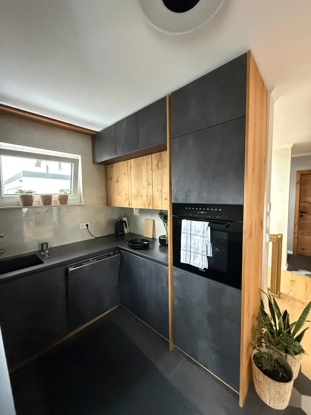 Moderne U-Küche mit anthrazitfarbenen Fronten in Betonoptik, Holzdekor, griffloser Einbauküche, hochgebautem Backofen und hochwertiger Küchenplanung.