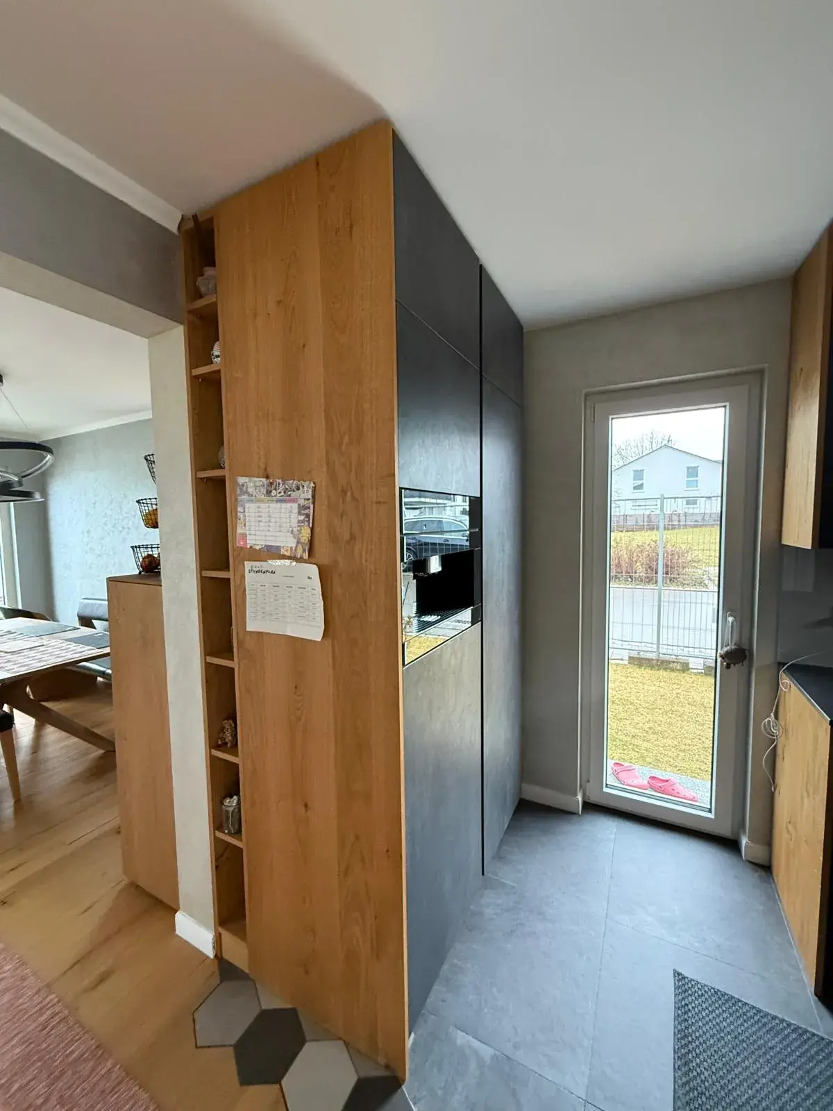 Moderne Designküche mit anthrazitfarbenen Fronten, Eichenholzoptik, grifflosen Hochschränken, offenem Regal und Terrassenzugang.