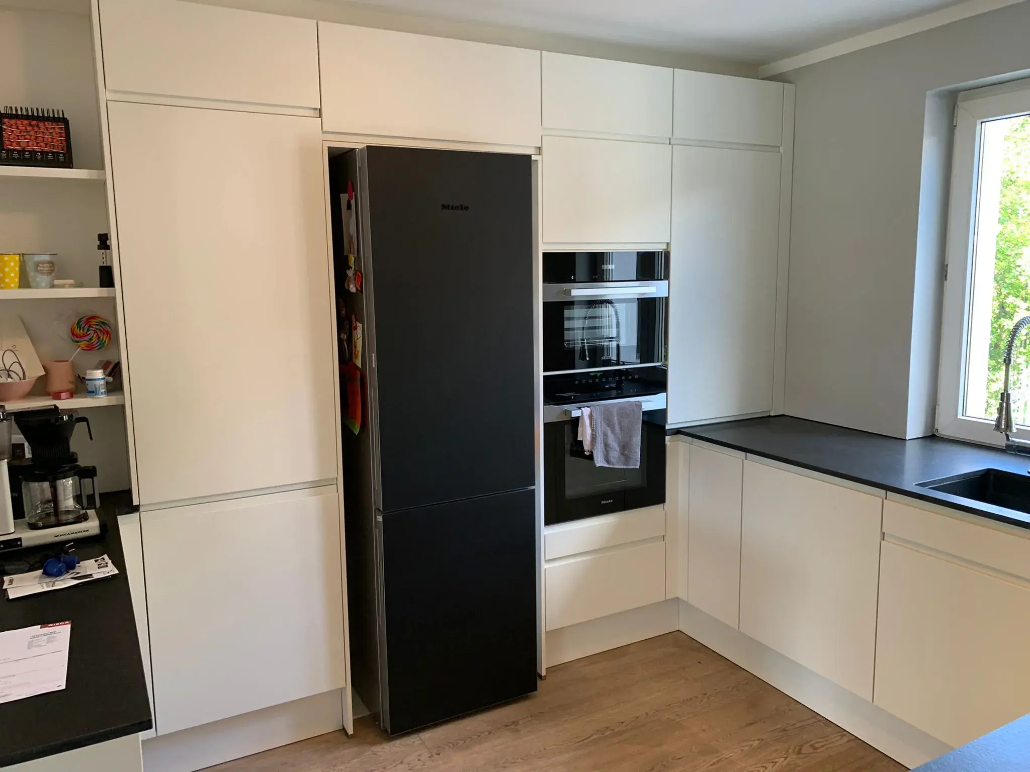 Moderne U-förmige Einbauküche mit weißen grifflosen Fronten, schwarzer Arbeitsplatte, Miele-Einbaugeräten und großzügigen Hochschränken.